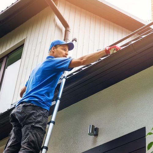 A Picture of a Man On a Ladder Cleaning Gutters.