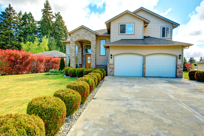 Big siding house with garage and high column porch. Green lawn with trimmed hedges and red bushes make the curb appeal stand out